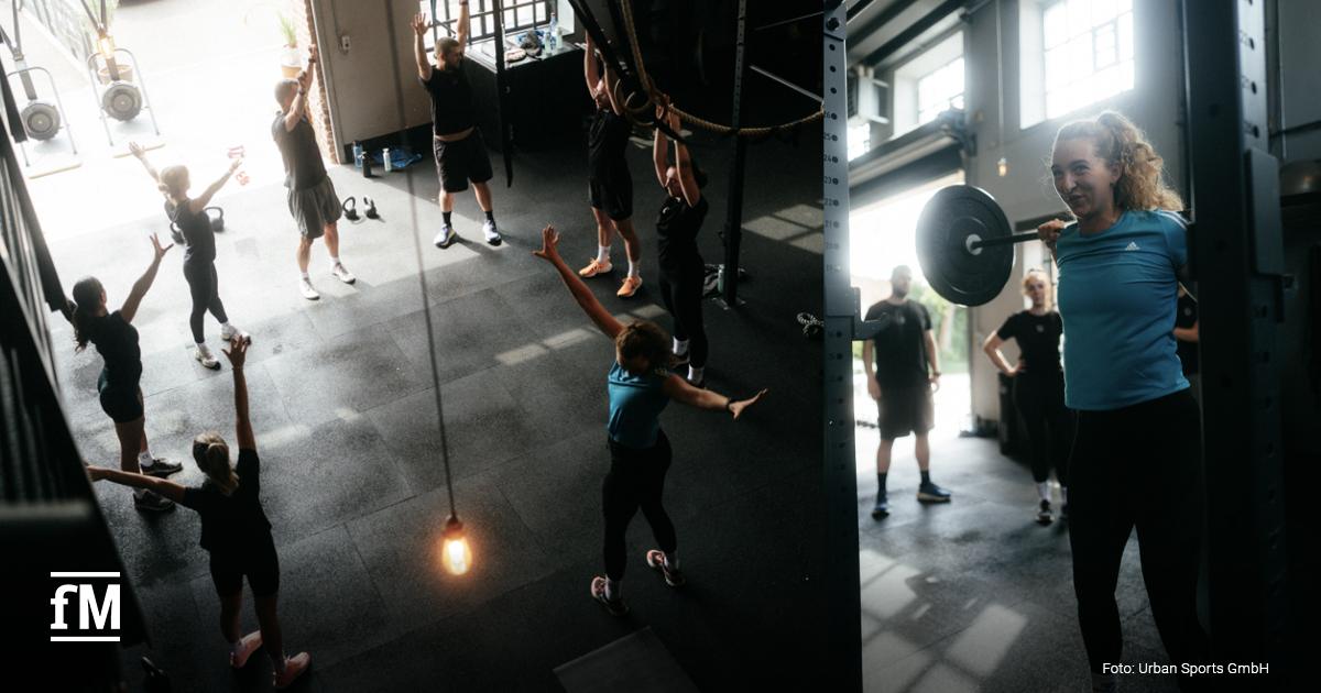 Mehrere Personen trainieren in einer Halle, von oben fotografiert, mit Fitnessgeräten und Seilen auf einer Trainingsfläche.