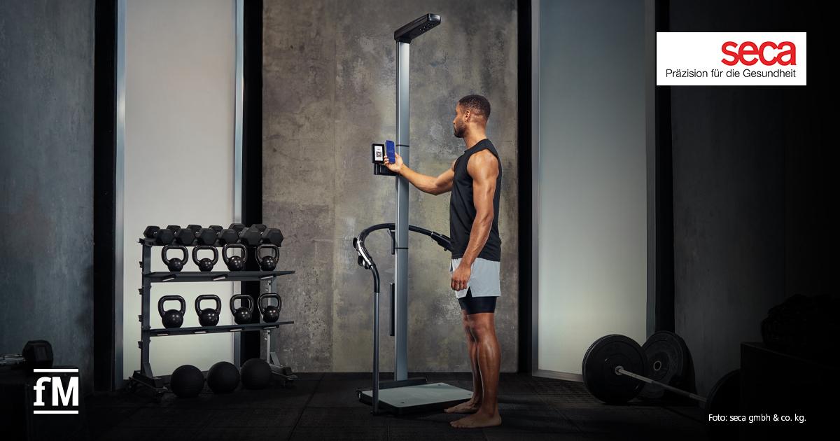 185 Jahre seca Sportler steht barfuß in einem Fitnessstudio an einer seca TRU und bedient das Display.