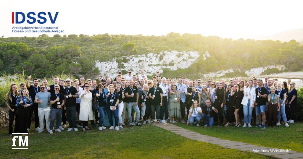 Große Gruppe von Menschen posiert im Freien vor einer Felslandschaft am Meer für ein Gruppenfoto.