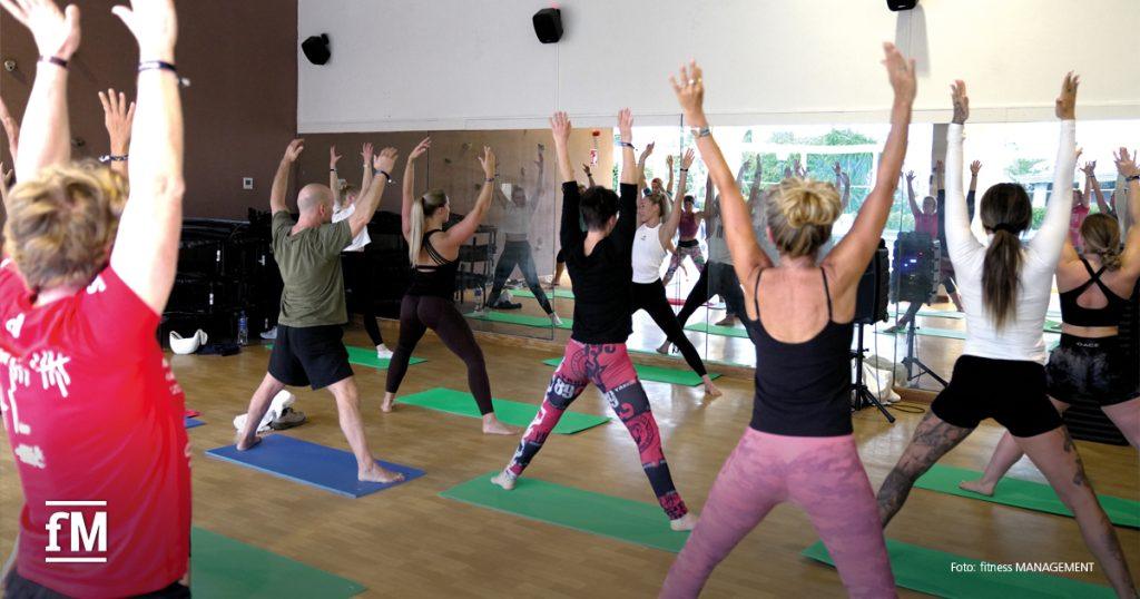 Personengruppe in Sportkleidung macht gemeinsam ein Workout in einem Fitnessraum mit Spiegelwand.