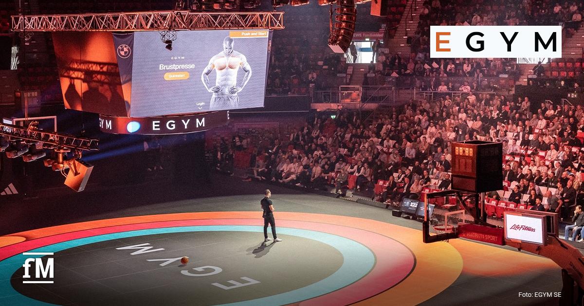 Große Konferenzbühne beim EGYM Kongress mit Präsentation, Moderator auf der Mitte der Arena und voll besetztem Publikum in einer Veranstaltungshalle.