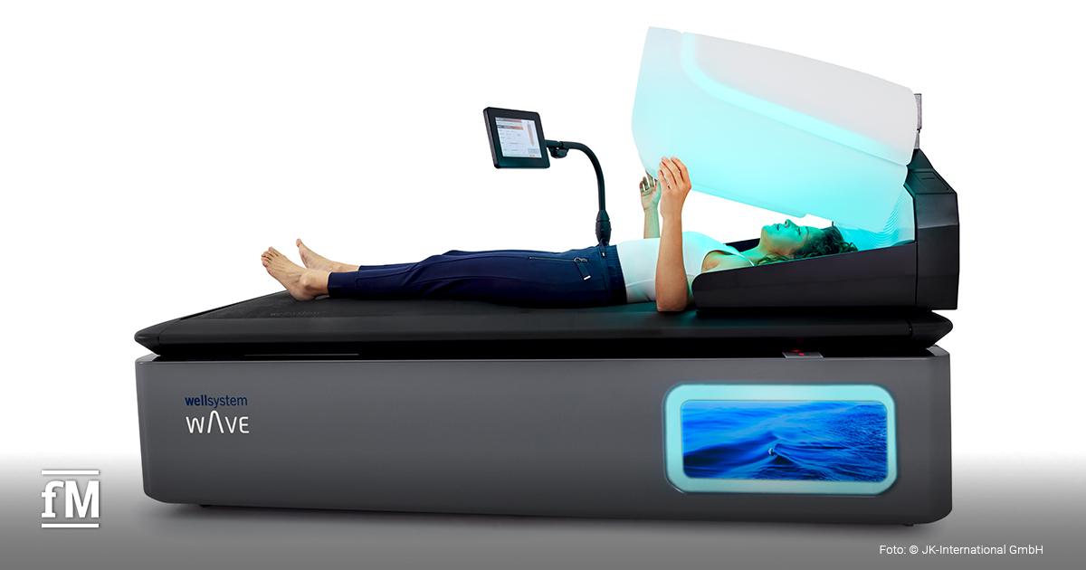 Person liegt auf dem wellsystem Hydrojet, während der obere Teil des Geräts mit blauem Licht geöffnet ist