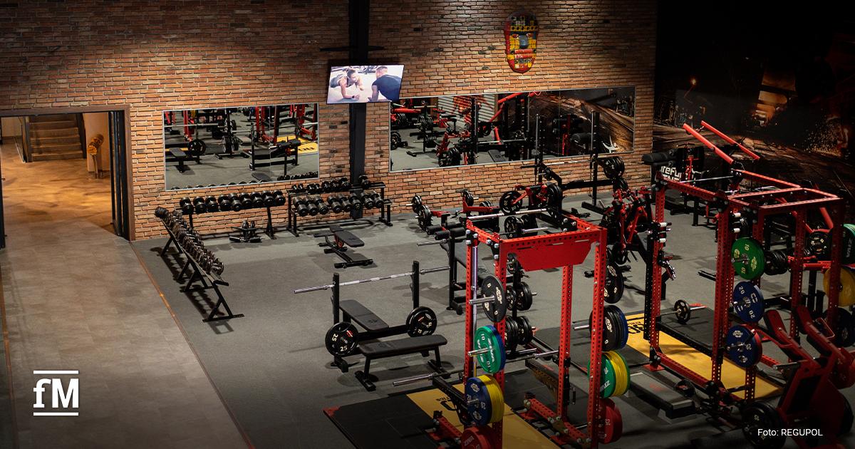 Krafttrainingsbereich mit Hanteln und Geräten auf grauem Fitnessboden.