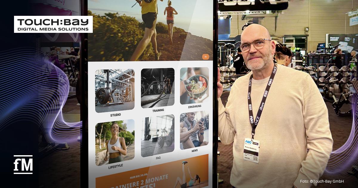 Digitale Stele mit TOUCH:BAY-Benutzeroberfläche neben einer Person in heller Kleidung in einer belebten Fitnessmessehalle.