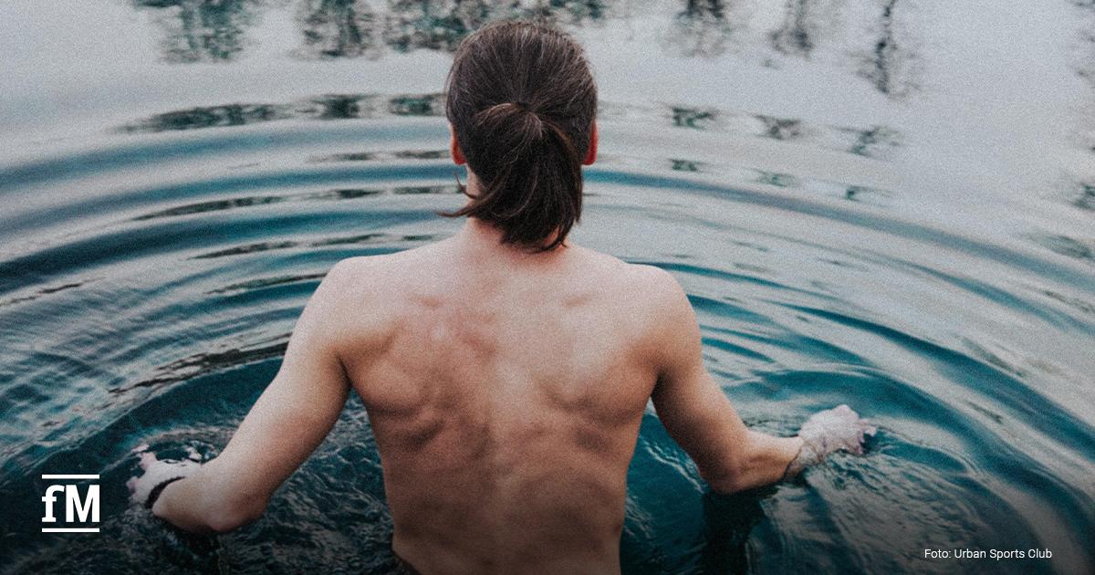 Oberkörperfreier Mann steigt rücklings in kaltes Wasser eines Sees.