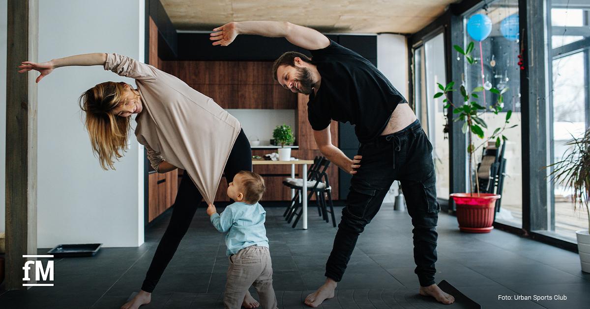 Mann, Frau und Kleinkind machen gemeinsam Sport in Wohnzimmerumgebung.