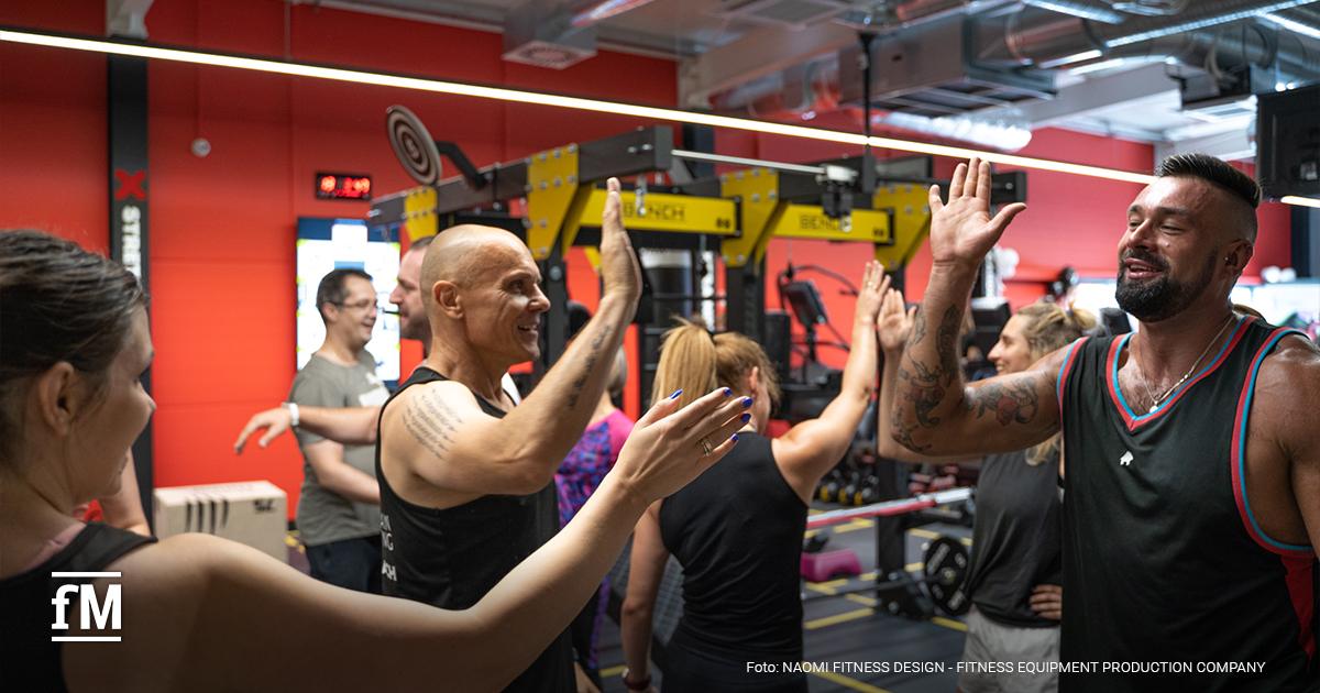 Mehrere Personen in Sportkleidung geben sich während einer Trainingseinheit in einem Fitnessstudio gegenseitig ein High Five.