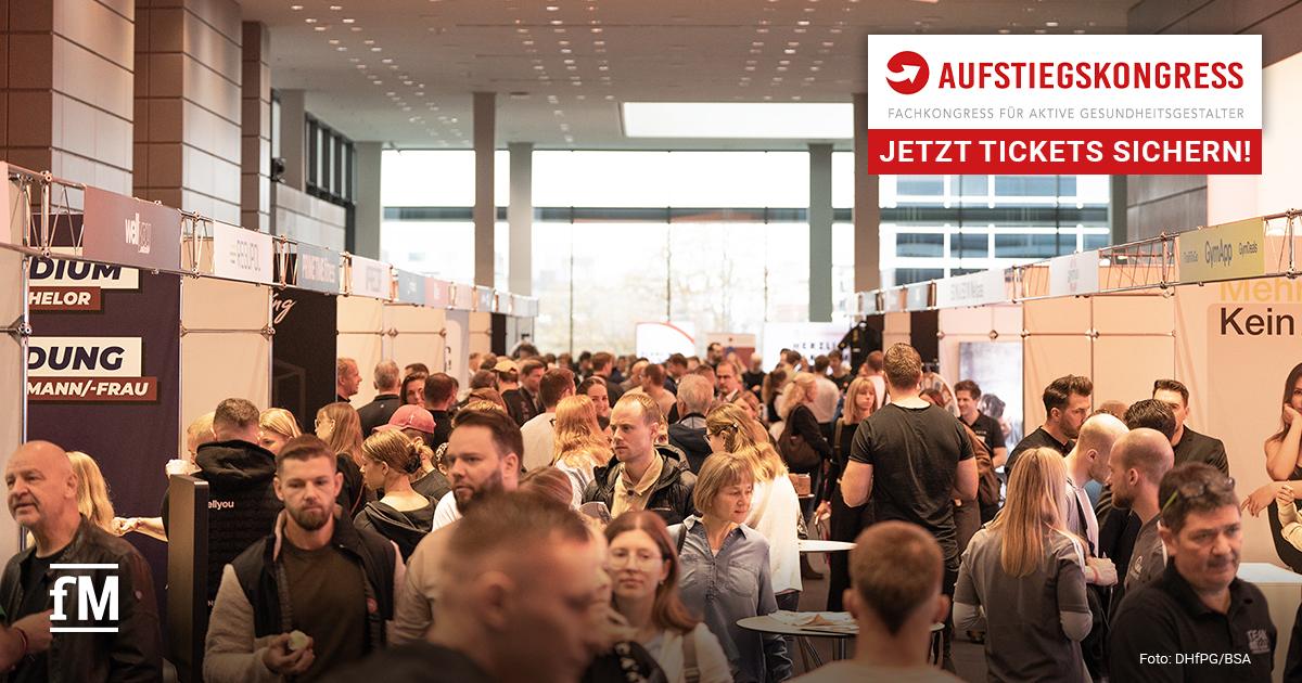 Besucherinnen und Besucher bewegen sich durch einen gut gefüllten Messegang mit zahlreichen Ausstellerständen in einer großen Kongresshalle.