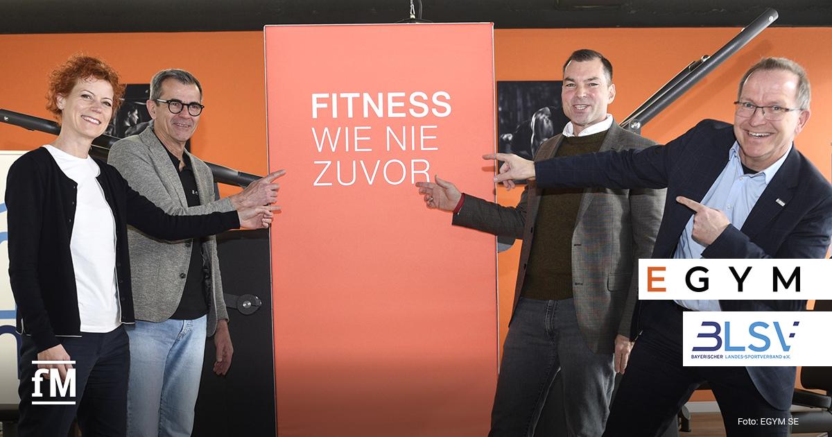 Vier Personen stehen in einem Trainingsraum vor Fitnessgeräten und zeigen auf einen Banner mit der Aufschrift 'Fitness wie nie zuvor', daneben sind die Logos von EGYM und dem BLSV zu sehen.