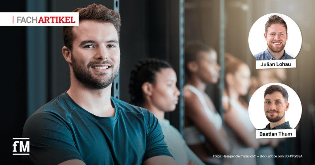 Ein Trainer steht mit verschränkten Armen im Vordergrund eines Fitnessstudios, im Hintergrund trainieren weitere Personen an Geräten
