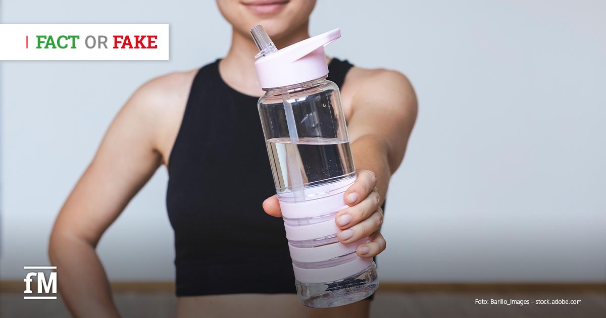 Person in Sportkleidung hält eine durchsichtige Trinkflasche mit Wasser in der Hand, Oberkörper und Arm sind sichtbar.