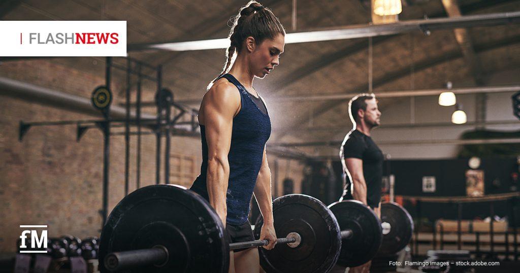 Zwei trainierende Personen heben Langhanteln in einem Fitnessstudio; im Vordergrund eine Frau in Sportkleidung, im Hintergrund ein Mann – beide konzentriert beim Kreuzheben.