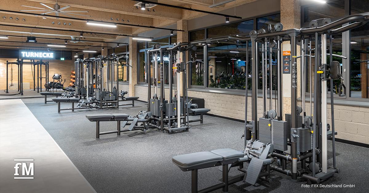 Trainingsbereich mit mehreren Kabelzugmaschinen und Hantelbänken in einem FitX-Studio