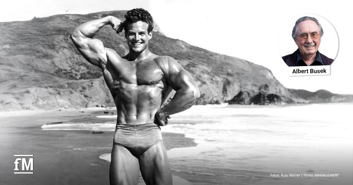 Albert Busek über Steve Reeves Schwarz-Weiß-Foto eines muskulösen Mannes in Badehose am Strand, der lächelnd den linken Arm anspannt, Meer und Felsen im Hintergrund.