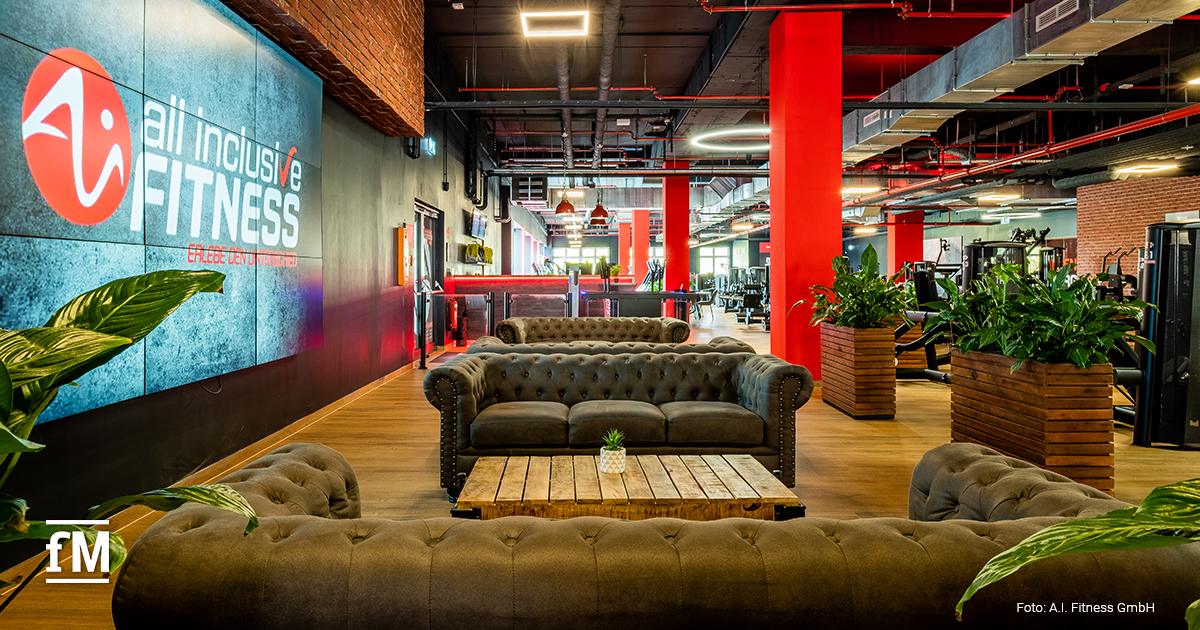 Lounge-Bereich im all inclusive Fitness-Studio mit Sofas, Holztisch, Pflanzen und Blick auf die Trainingsflächen