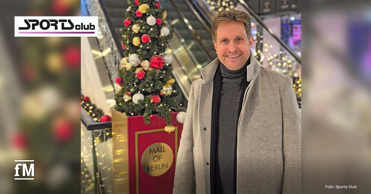 Ein Mann (Sports Club Geschäftsführer Alexander Sosa) in grauem Mantel steht neben dekoriertem Weihnachtsbaum in der Mall of Berlin, im Hintergrund Rolltreppen und Lichterdekoration.