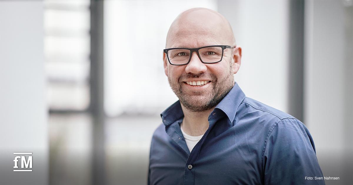 Mann mit Brille und Bart in Anzug und Krawatte vor hellem, unscharfem Hintergrund in einem Innenraum