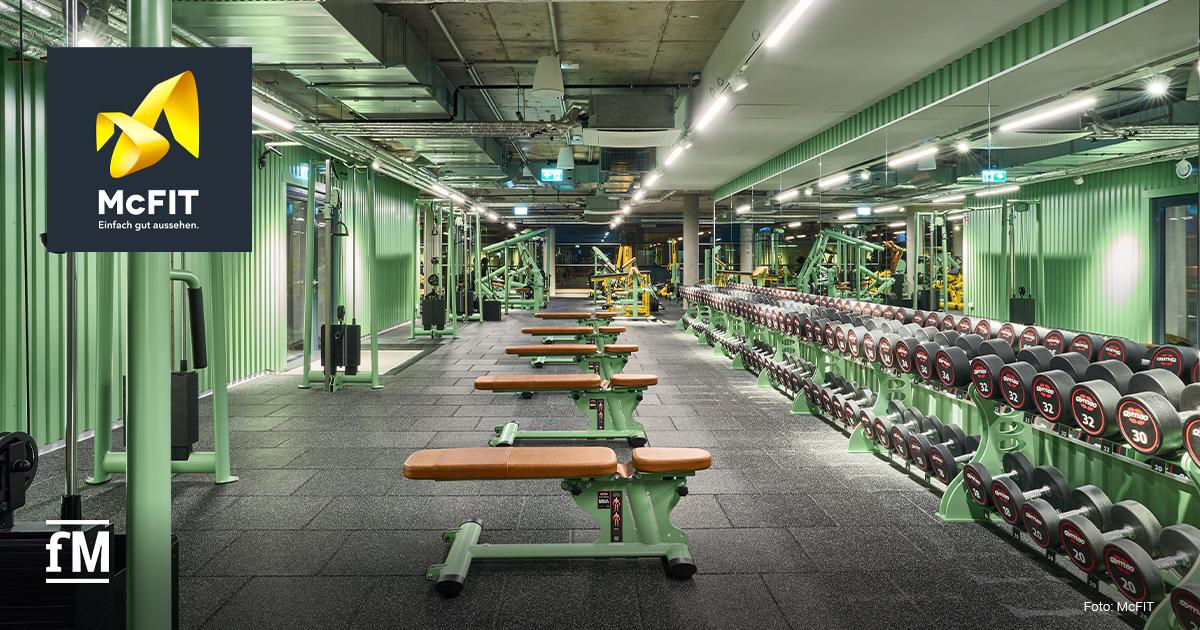McFIT Frankfurt Zeil Innenansicht eines Fitnessstudios mit grünen Wänden, Hantelregal, Trainingsbänken, Kraftgeräten und McFIT Logo links oben.