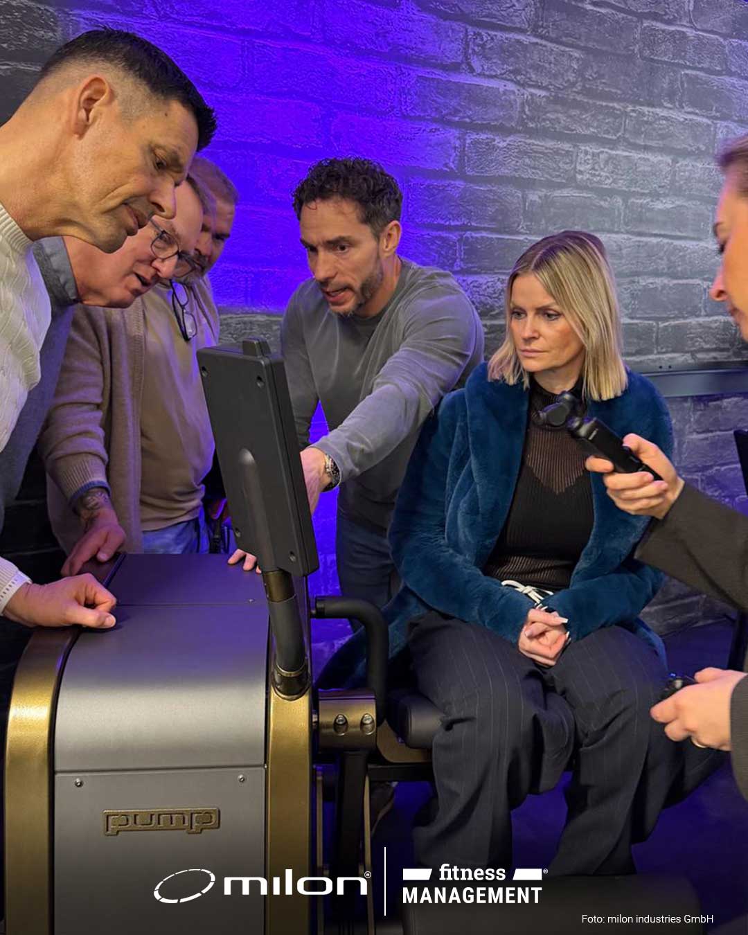 Mehrere Personen beugen sich über einen Bildschirm an einem Trainingsgerät in einem Raum mit grauer Wand.