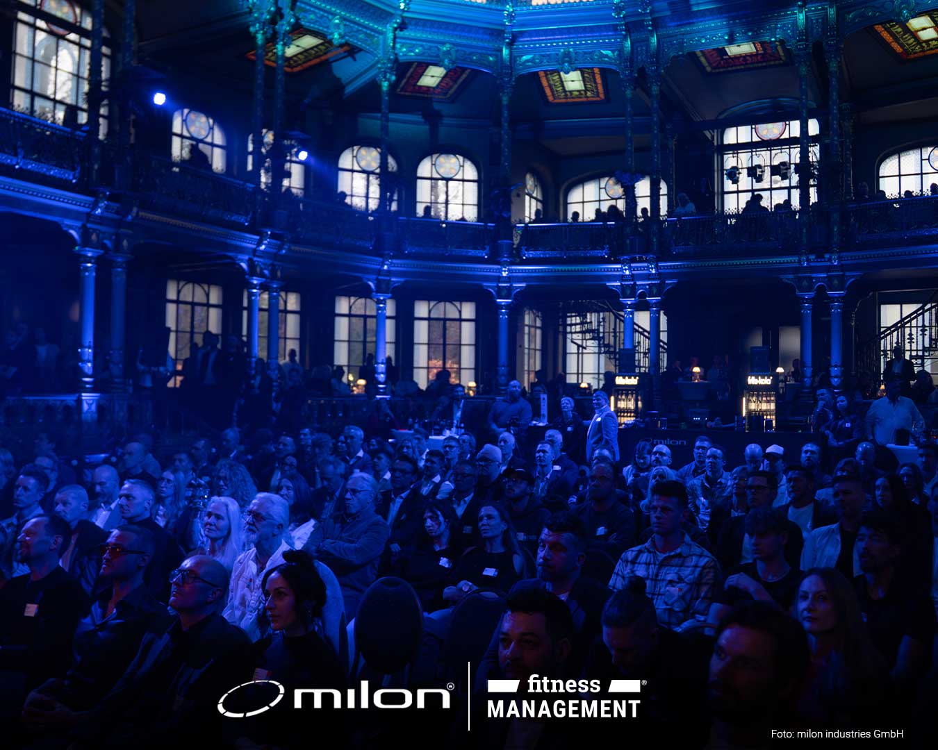 roßer Saal mit Balkon und Rundbögen, viele sitzende Personen schauen Richtung Bühne.