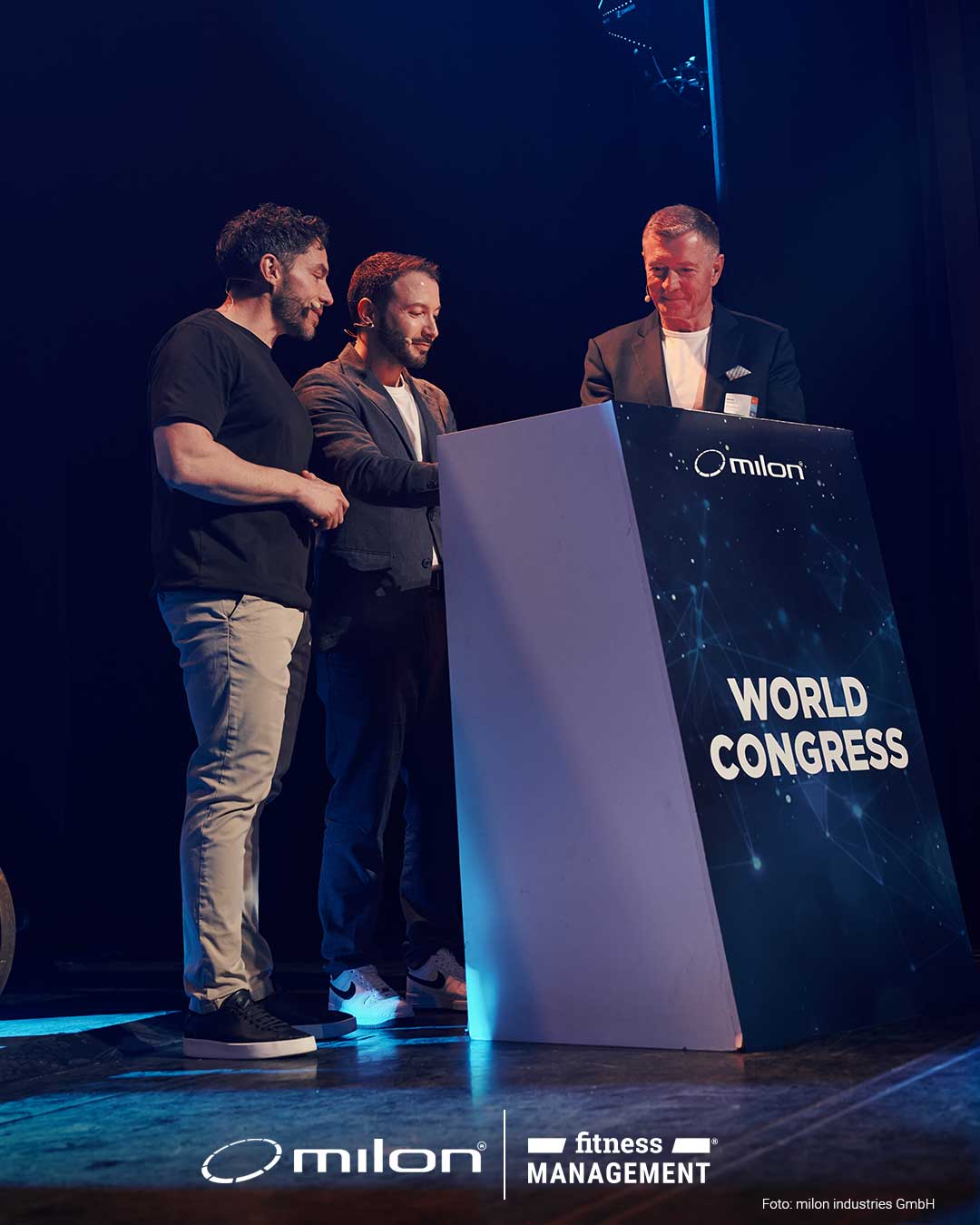 Drei Männer stehen hinter einem Rednerpult mit der Aufschrift „WORLD CONGRESS“ auf einer Bühne