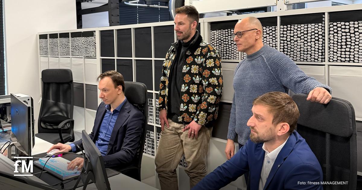 Büroarbeitsplatz mit mehreren Monitoren, zwei Männer sitzen vor Bildschirmen mit technischer Planung, zwei weitere stehen dahinter.