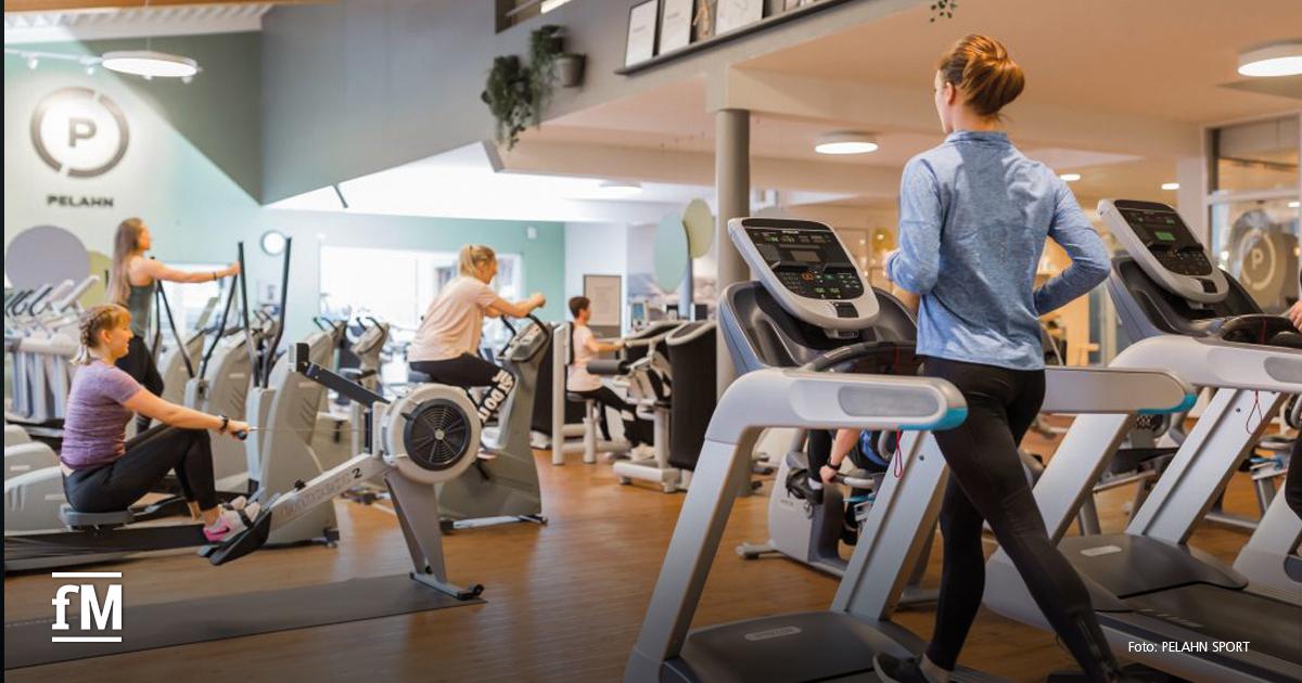 Mehrere Personen trainieren auf Laufbändern, Rudergeräten und Cardiogeräten in einem hellen Fitnessstudio mit Holzfußboden.