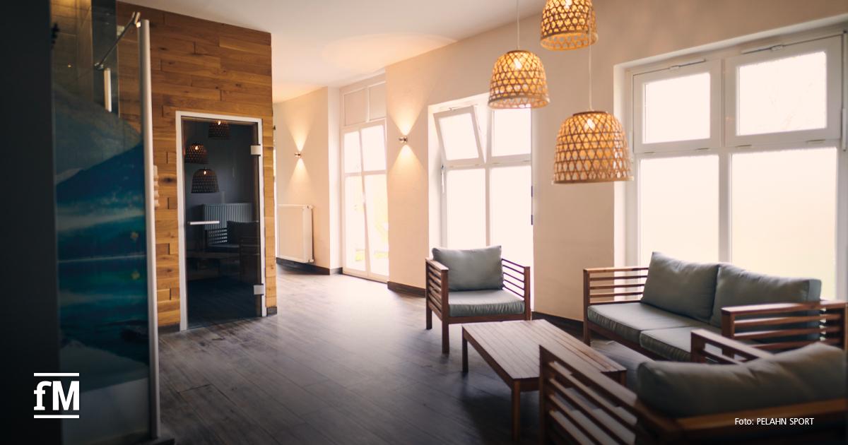 Saunaeingang mit Holzverkleidung, Sitzmöbeln und großen Fenstern in einem hellen Raum.