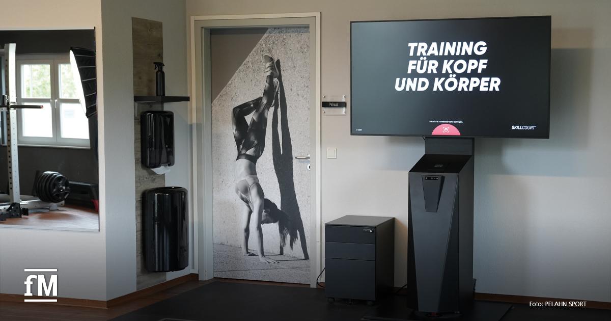 Trainingsfläche mit markierten Feldern am Boden, Bildschirm mit Schriftzug „Training für Kopf und Körper“ und SKILLCOURT-System an der Wand.