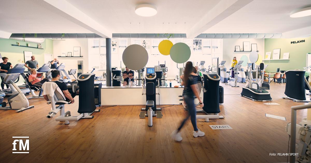 Große Fitnessfläche mit Kraft- und Cardiogeräten, mehreren trainierenden Personen und Holzfußboden.