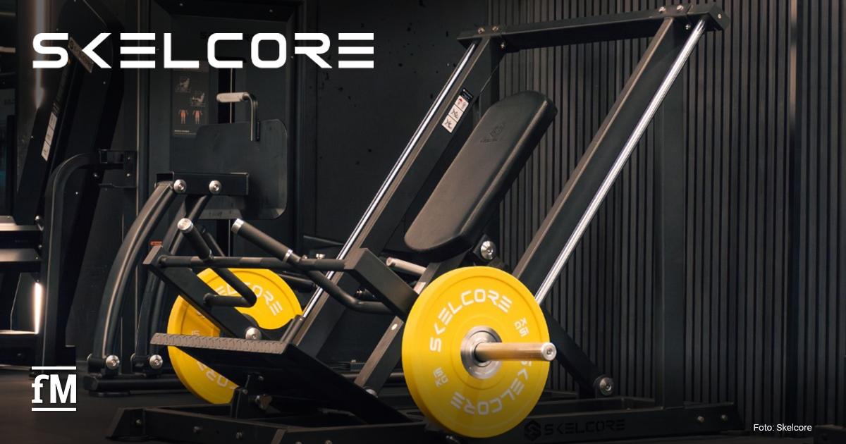 Skelcore 2.0 Schwarze Beinpresse mit gelben 15kg Skelcore-Gewichtsscheiben, schwarzer Wandverkleidung und Skelcore-Logo oben links im Bild.