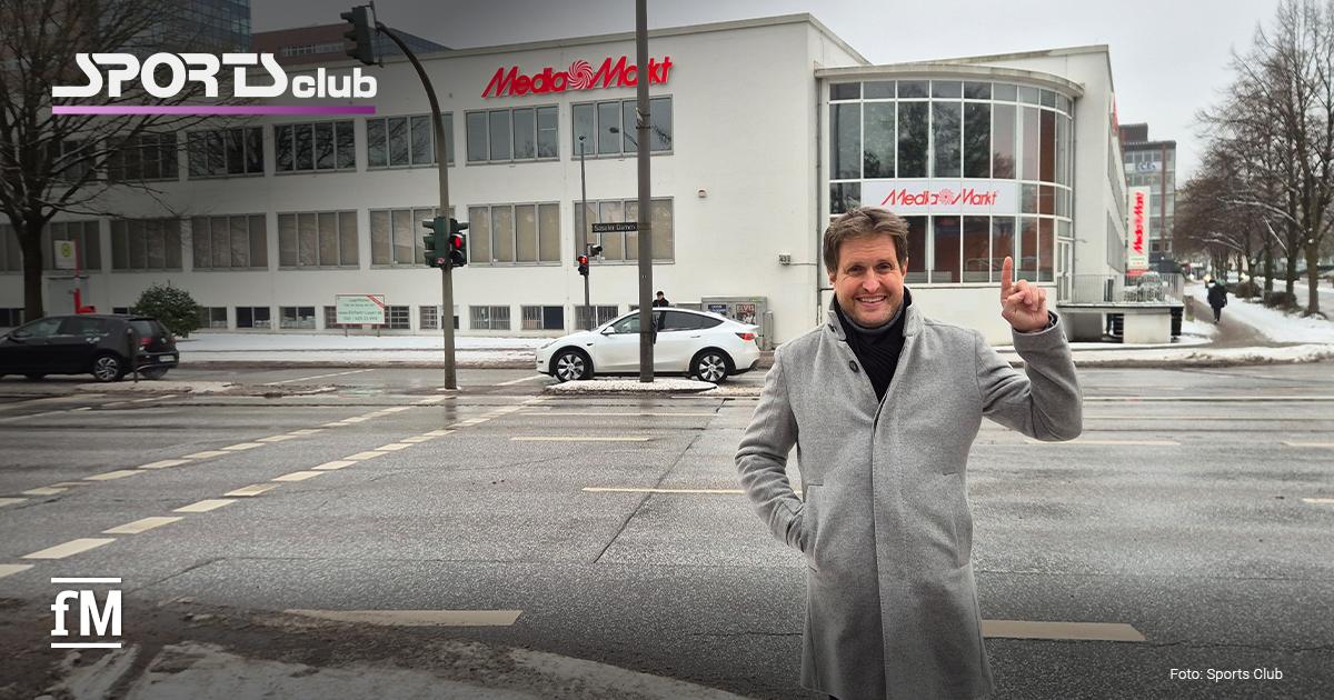Straßenkreuzung am Saseler Damm in Hamburg-Poppenbüttel mit weißem Eckgebäude und Media-Markt-Schriftzug, davor steht Alexander Sosa im grauen Mantel auf dem Gehweg.