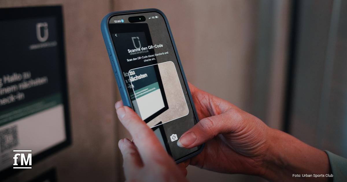 Innenraum eines Studios, eine Person hält ein Smartphone und scannt einen QR-Code an einem Terminal