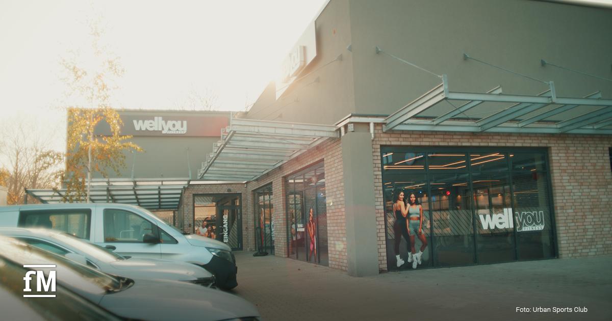 Gebäude mit wellyou Beschriftung, Glasfassade, parkende Autos im Vordergrund