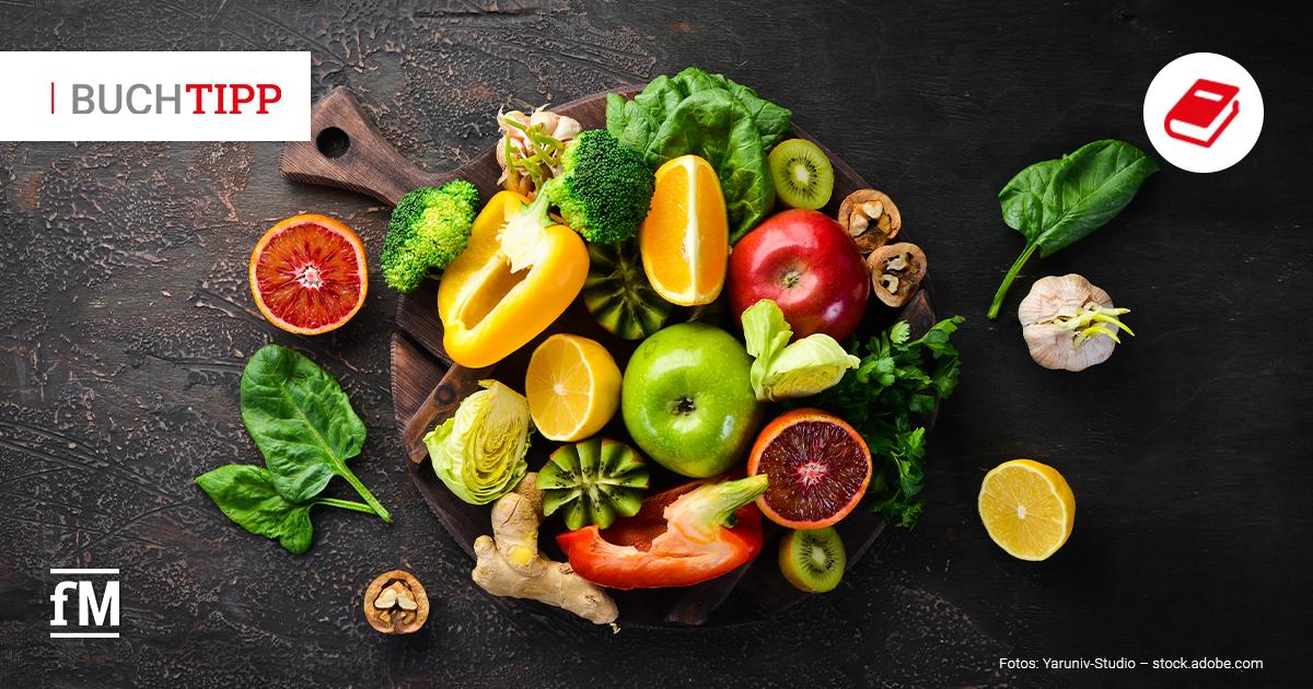 Buchtipp „Der Vitaminkompass“ Bas Kast Draufsicht auf dunkle Tischoberfläche mit Holzbrett, darauf Brokkoli, Paprika, Zitrusfrüchte, Apfel, Kiwi, Spinat, Ingwer und Nüsse verteilt.