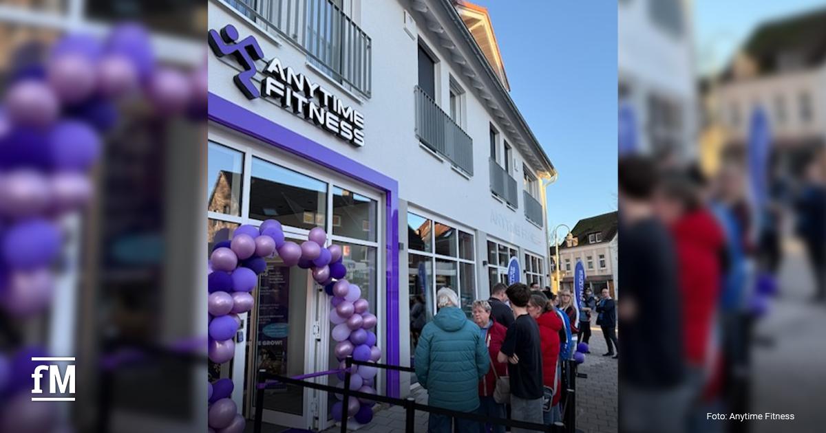 Gebäude mit Anytime Fitness Logo über dem Eingang, lila Ballonbogen und mehrere Personen vor dem Eingang auf dem Gehweg.