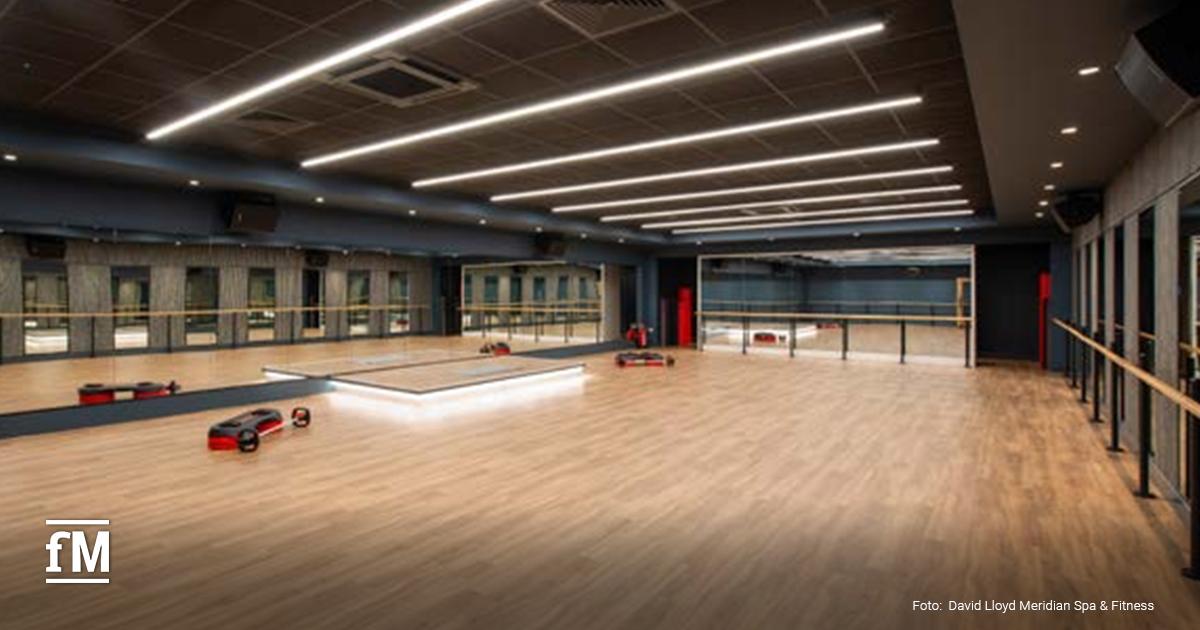 Großer Fitnessraum mit Laufstrecke auf dem Boden, Kraftgeräten und Pflanzen.