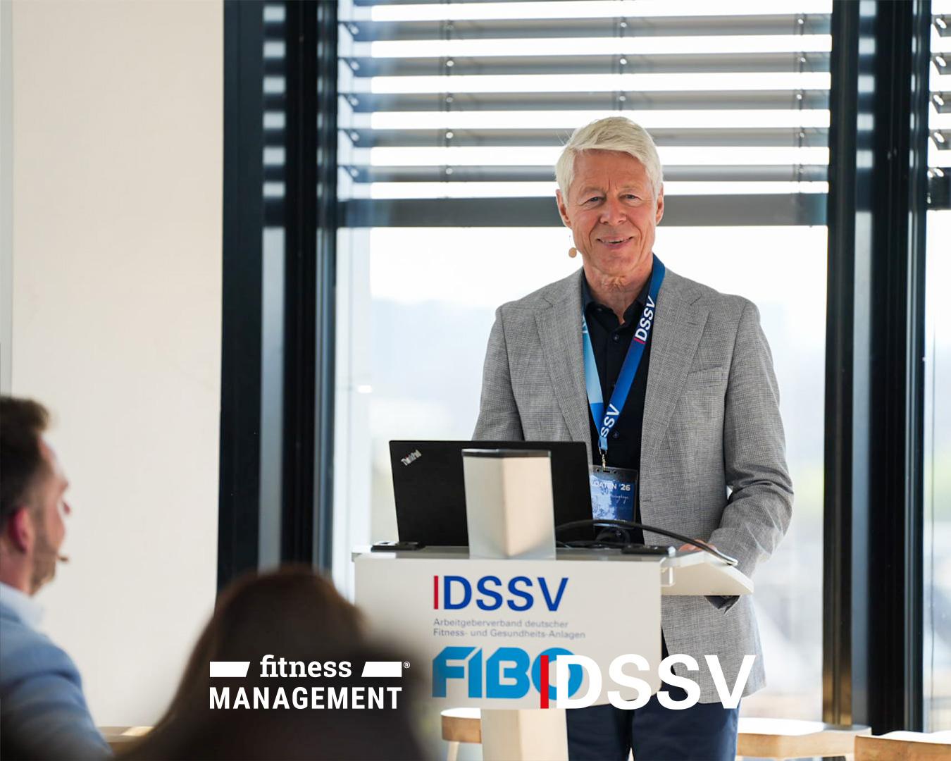 Ein Mann steht an einem Rednerpult und spricht zu einem Publikum, vor ihm ein Laptop und ein DSSV-Logo