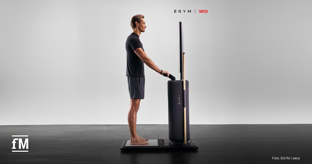 EGYM Fitness Hub seca edition Ein Mann steht barfuß auf der Messplattform des EGYM Fitness Hub seca edition und hält die Handgriffe für eine integrierte seca Körperanalyse.
