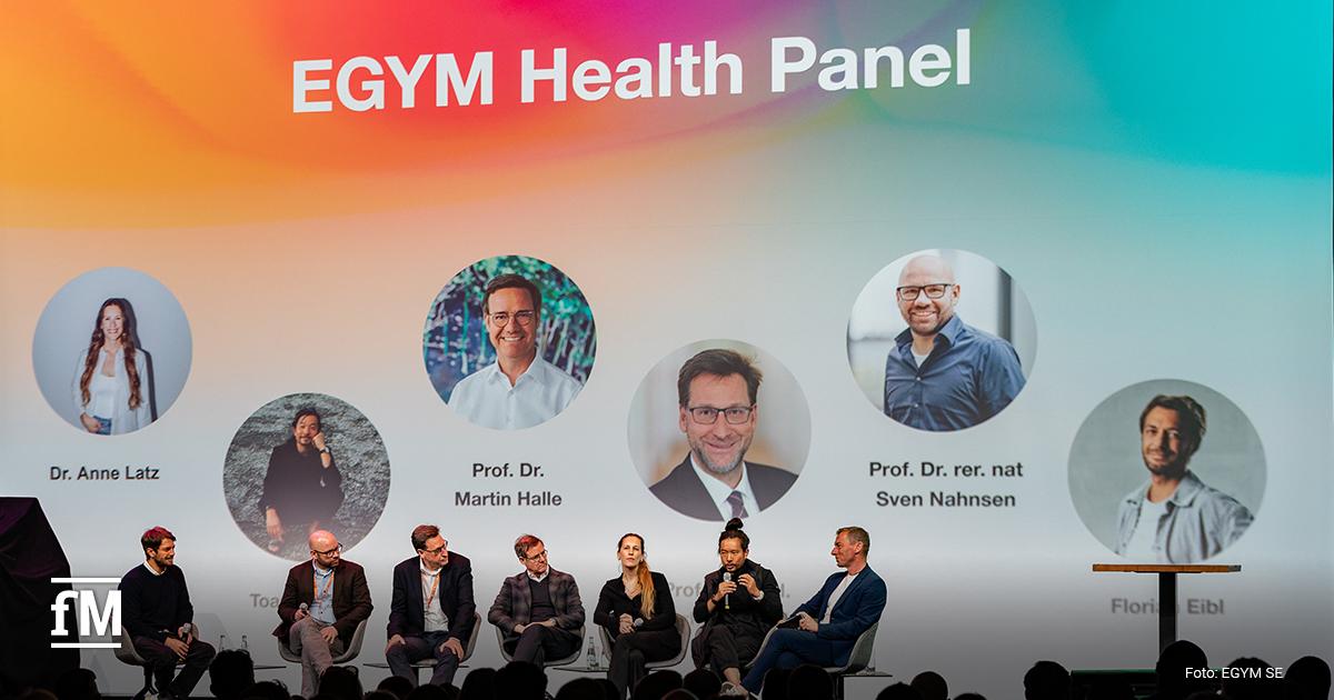 Mehrere Personen sitzen auf Bühne in einer Diskussionsrunde vor Leinwand mit Titel „EGYM Health Panel“ und Porträts der Teilnehmenden