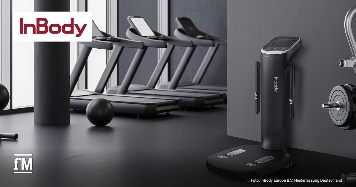 Schwarzes InBody Black Edition Körperanalysegerät steht in einem Fitnessstudio neben Laufbändern, einem Gymball und einer Hantelstange.