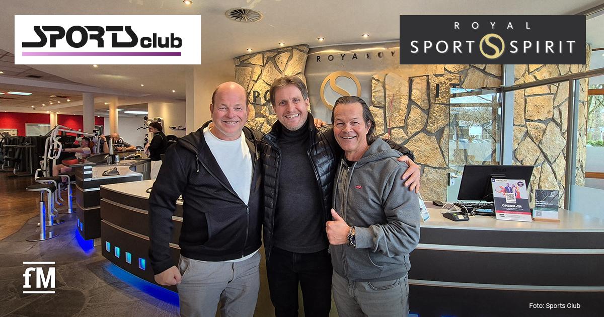 Sports Club übernimmt das Royal Sports Spirit Hamburg Drei lächelnde Männer stehen Arm in Arm im Empfangsbereich eines Fitnessstudios. Im Hintergrund sind Rezeption, Trainingsgeräte und Steinwände zu sehen; oben eingeblendet sind die Logos Sports Club und Royal Sports Spirit.