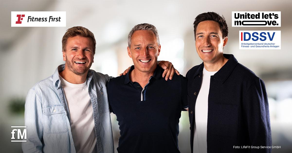 Übergabe „United let’s move.“ Fitness First Drei Männer stehen nebeneinander vor hellem Hintergrund. Die Person in der Mitte legt jeweils einen Arm auf die Schultern der Männer links und rechts. Alle blicken frontal zur Kamera.