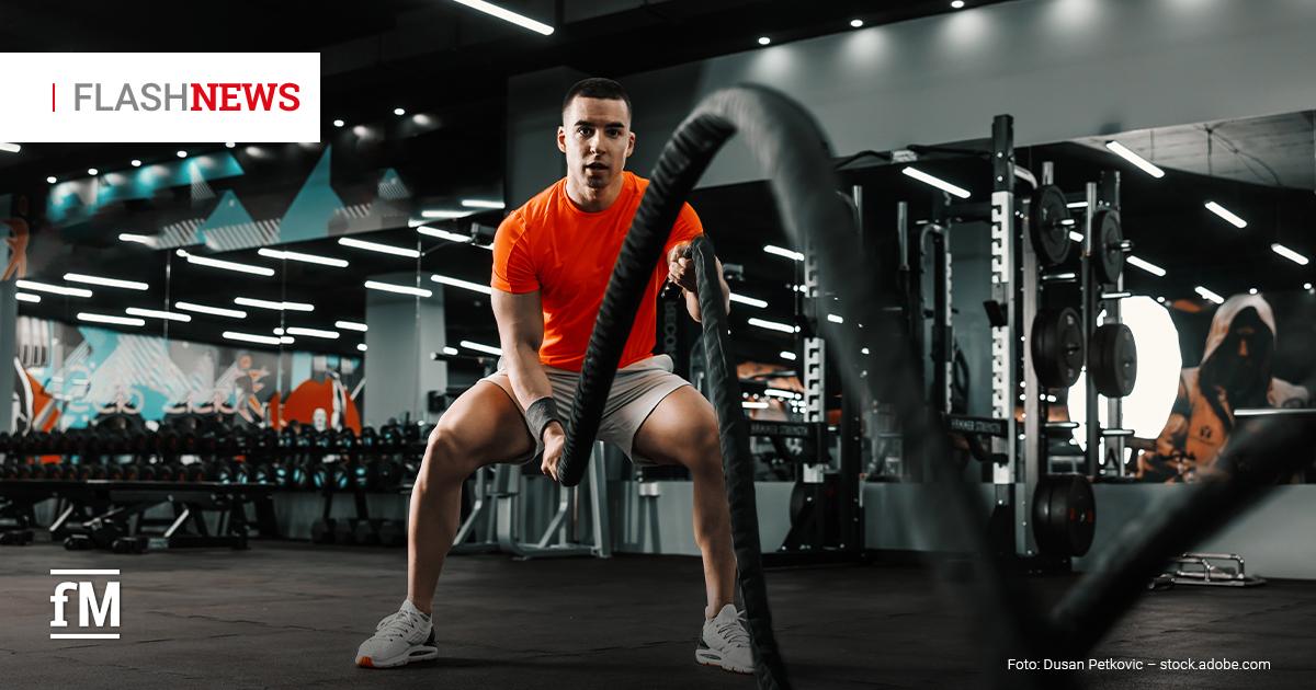 Fitness Flash News #04/2026 KW 17 Mann im Fitnessstudio macht Battle-Rope-Übung, trägt rotes Shirt und helle Shorts; im Hintergrund Hanteln und Trainingsgeräte, oben links Schriftzug „FLASH NEWS“.