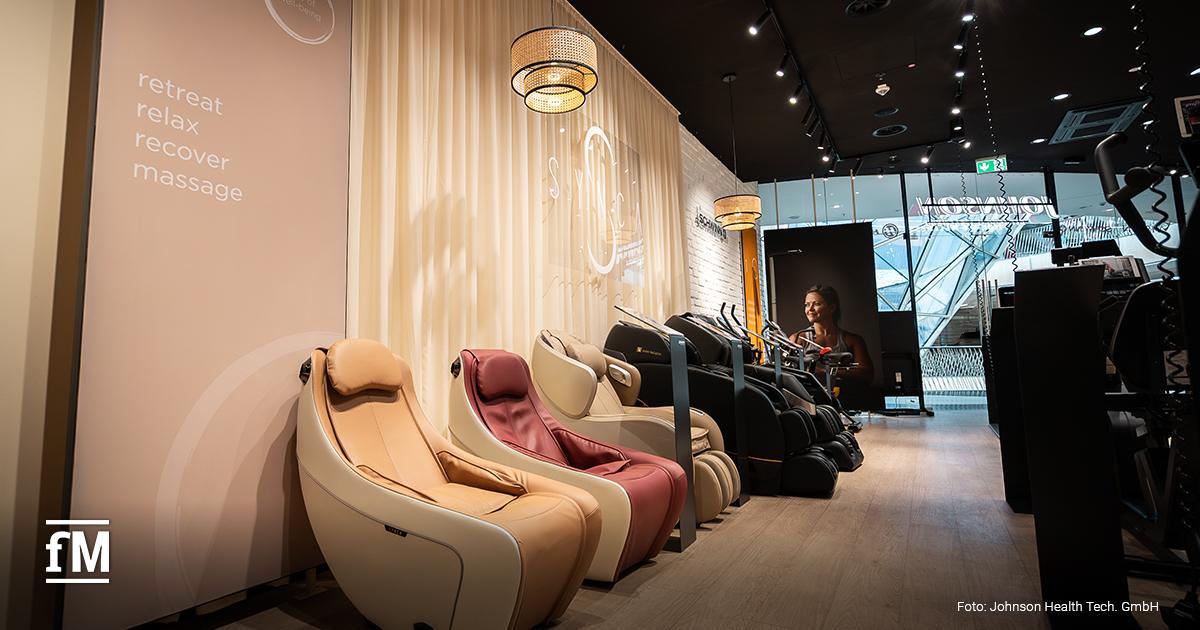 Reihe von Massagesesseln entlang eines hellen Vorhangs im linken und mittleren Bildbereich, links an der Wand die Wörter „retreat“, „relax“, „recover“ und „massage“.