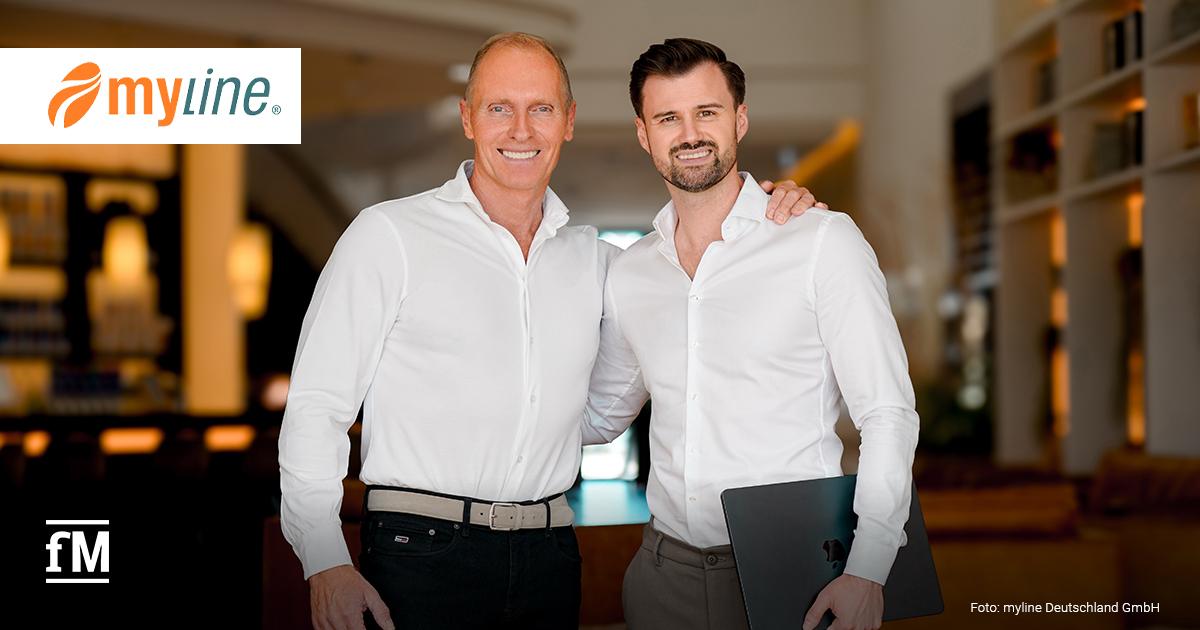 Zwei Männer in weißen Hemden stehen mittig in einem Innenraum; der linke legt den Arm um die Schulter des rechten, der rechte hält einen dunklen Laptop unter dem Arm. Oben links das Logo „myline“, unten links das Logo „fM“, unten rechts der Schriftzug „Foto: myline Deutschland GmbH“; im unscharfen Hintergrund Regale und warmes Licht.