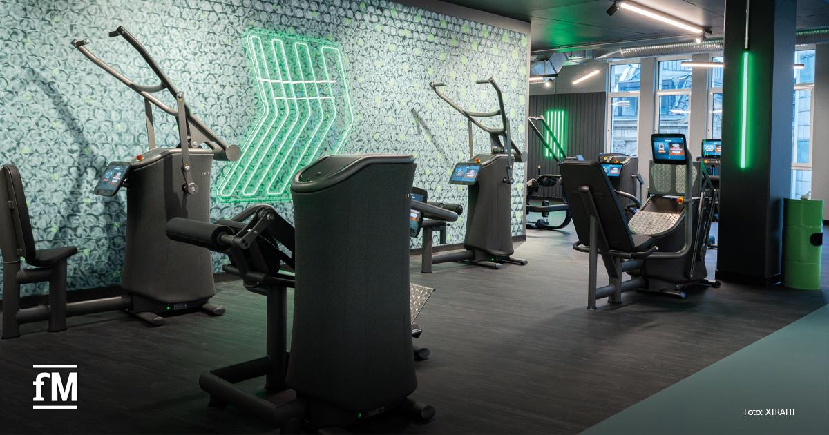 Moderner Gerätebereich im XTRAFIT Köln-Zentrum mit digitalisierten Kraftmaschinen, Neon-Wandgrafik und dunklem Interior.