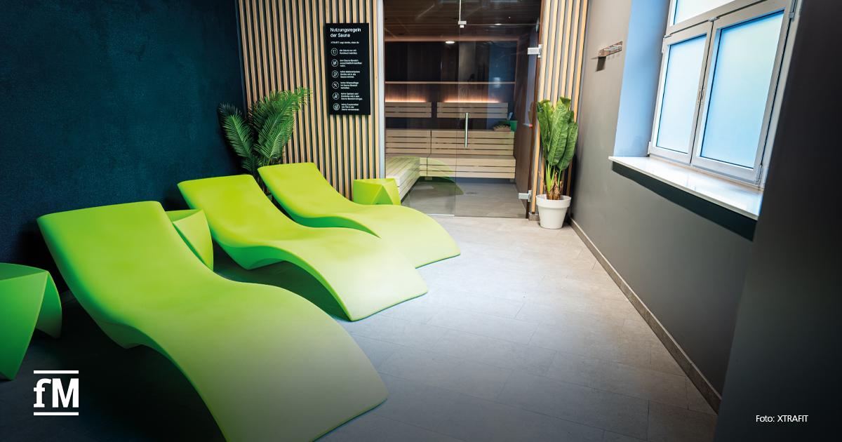 Wellnessbereich mit grünen Liegen, Holzlamellen, Pflanzen und Blick auf den Saunabereich im XTRAFIT Köln-Zentrum.