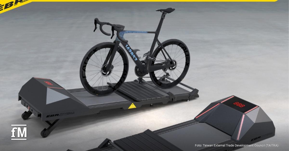 Ein Rennrad steht auf einer mehrteiligen Plattform mit Rollen und Sensorik, im Vordergrund weitere modulare Elemente, neutraler Studiohintergrund.