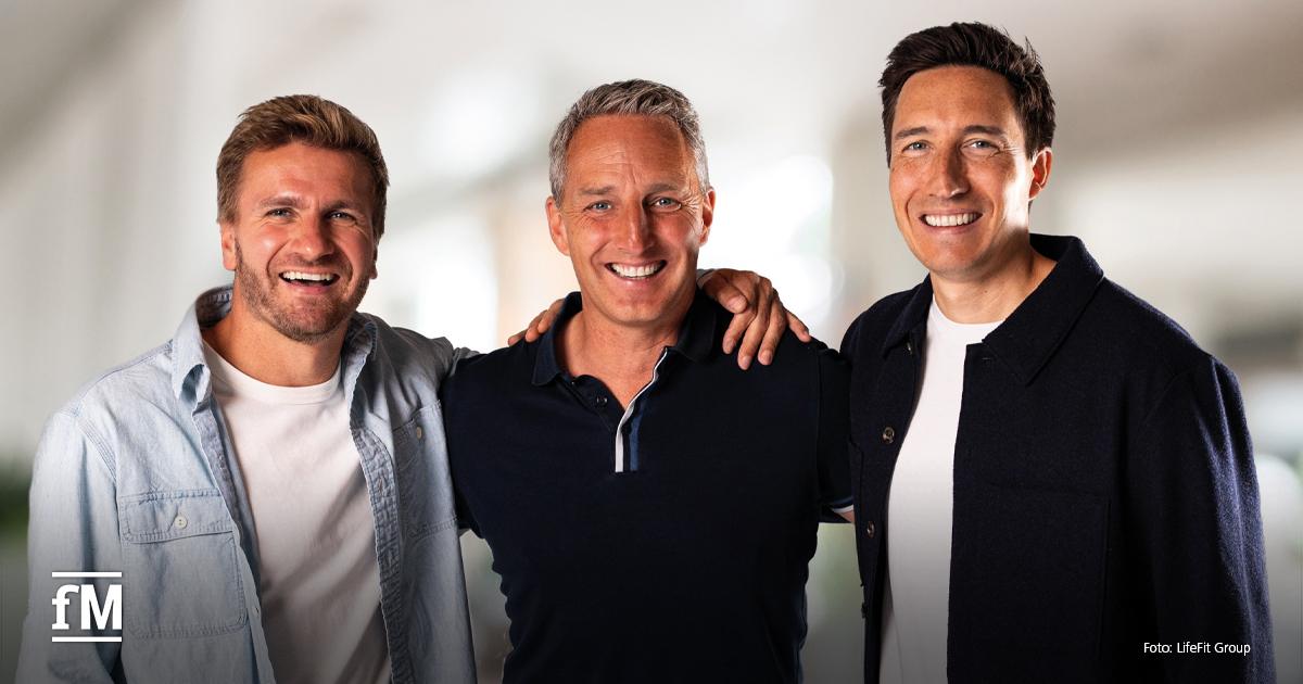 Drei Männer (Johannes Maßen, Martin Seibold und Christophe Collinet) nebeneinander, lächelnd, mittlere Perspektive, Hände auf Schultern, heller Hintergrund, unten links Logo „fM“, unten rechts Text „Foto: LifeFit Group“.